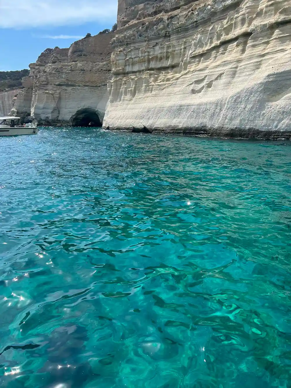Clear green water below a white cliff with a tunnel