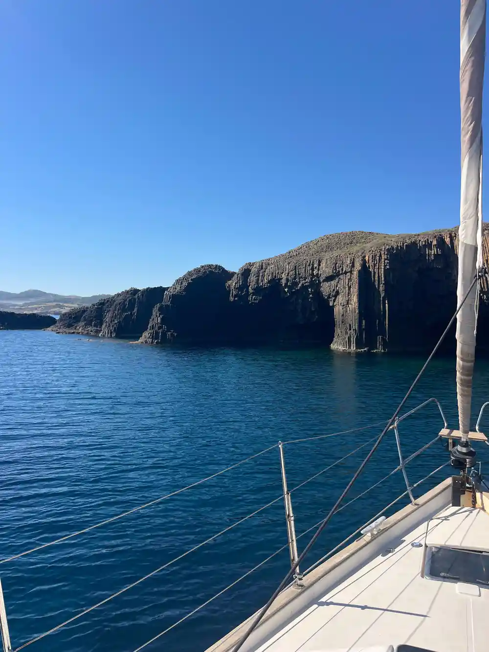 Dark cliff with a cave mouth at the waterline seen from a yacht