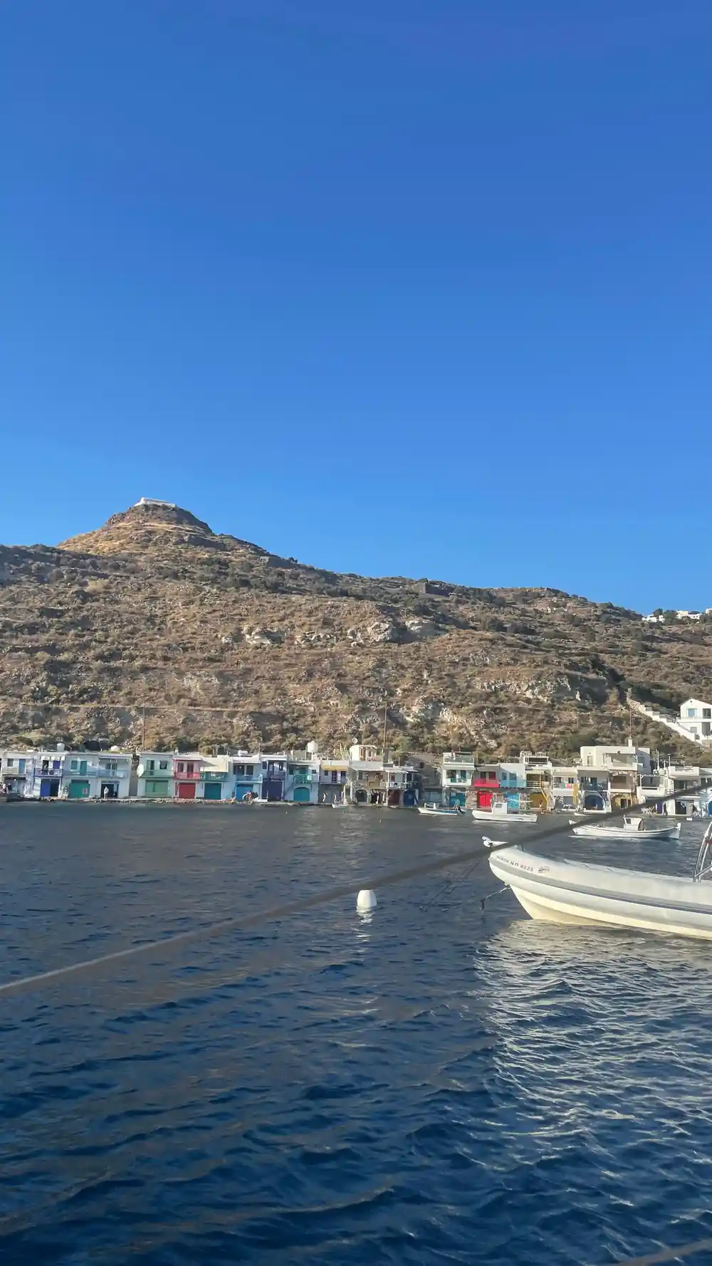Painted boathouses along the quay below a hill