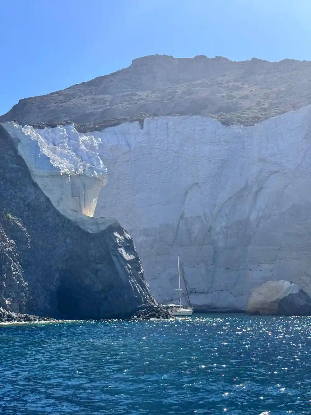Sheer white cliff with a yacht dwarfed below it