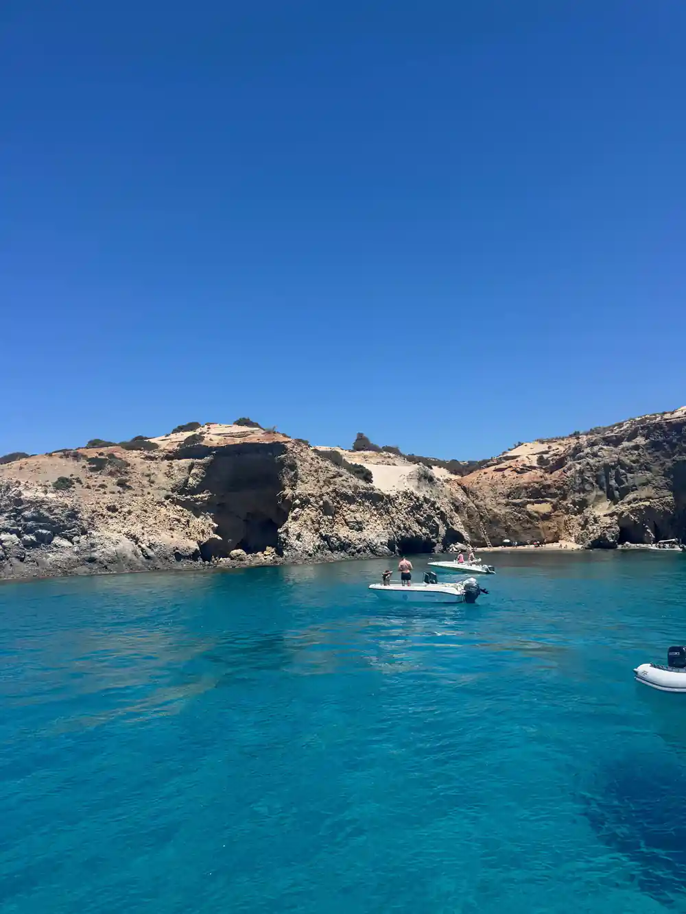 Small boat anchored in a turquoise bay below an eroded headland