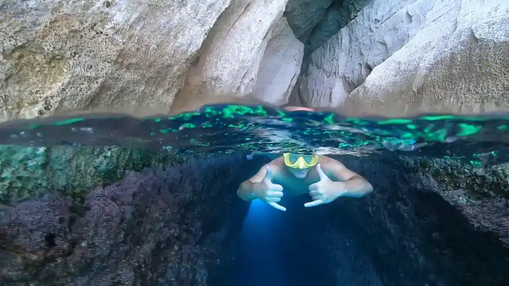 Split shot of a swimmer beneath a rock overhang