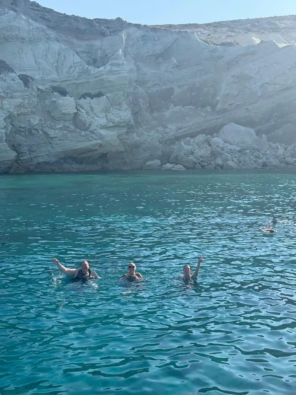 Swimmers in clear shallow water below a white rock face