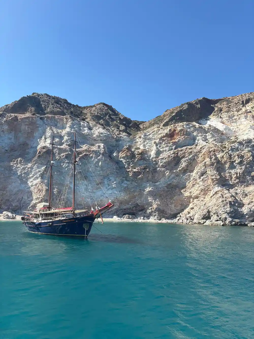 Traditional wooden schooner anchored below white rock