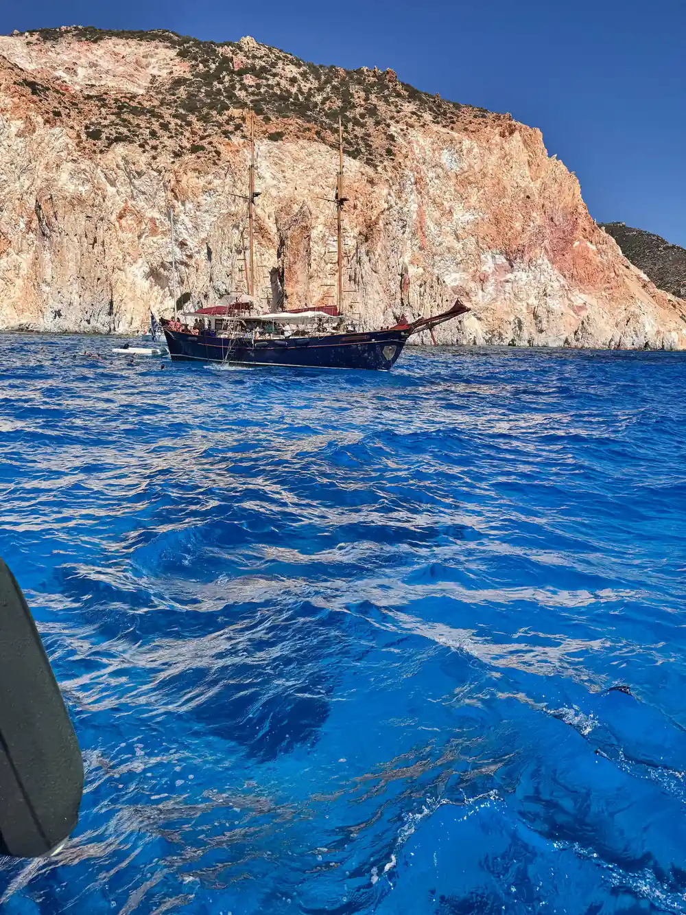 Wooden schooner anchored under a red and white cliff
