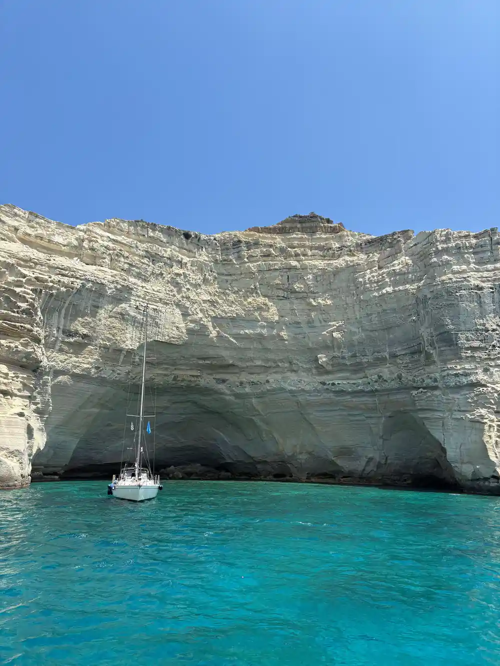 Yacht anchored beneath an overhanging white cliff