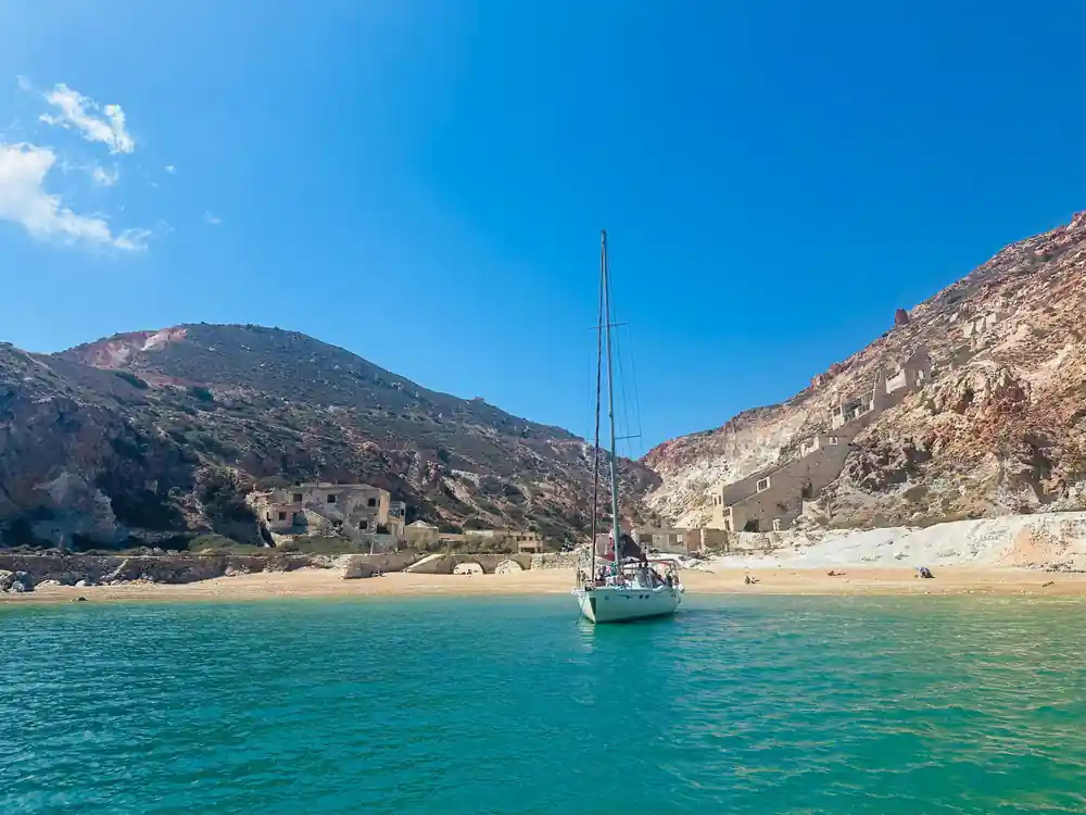 Yacht anchored off a sandy beach with ruined buildings behind
