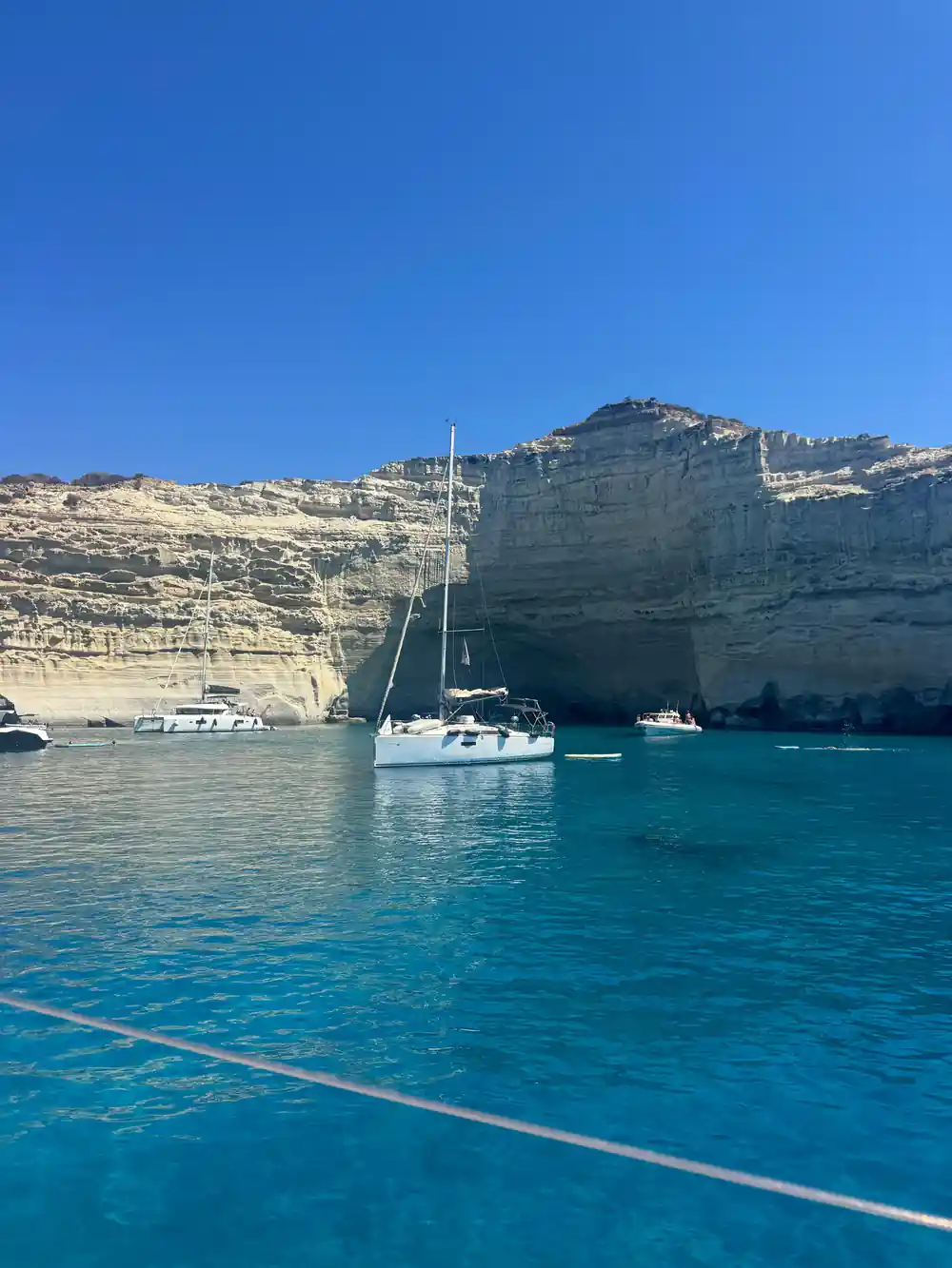Yachts anchored under layered white cliffs with cave openings