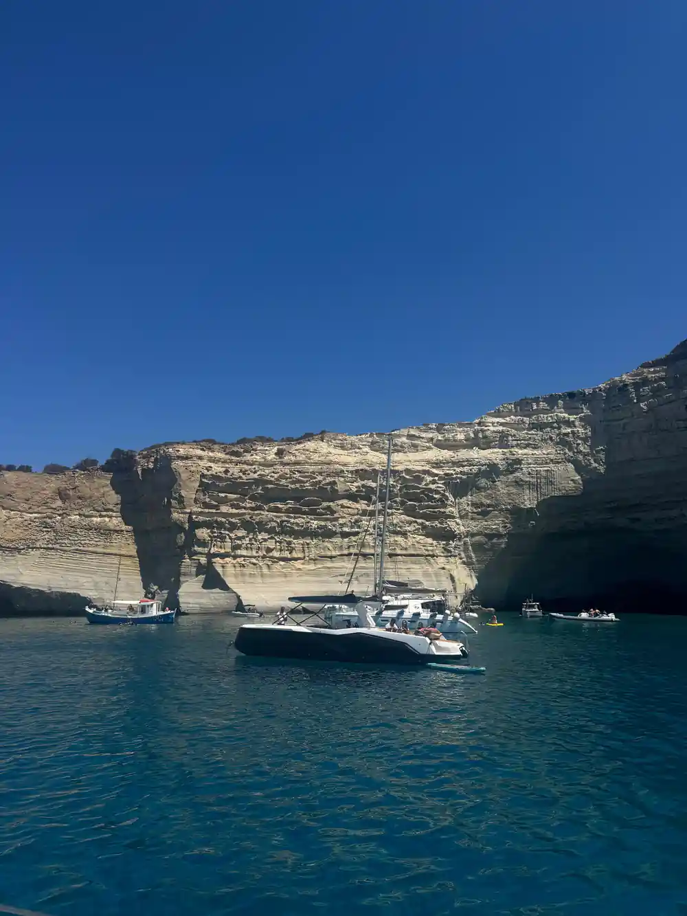 Yachts below a pale cliff with a rock pillar and cave mouths